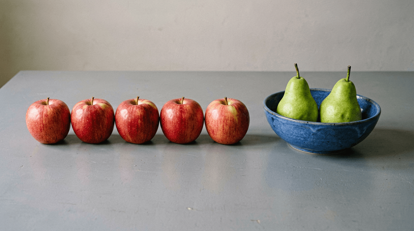 ERNIE-Image Turbo studio photo of five red apples in a row on a grey table beside a blue ceramic bowl holding two green pears